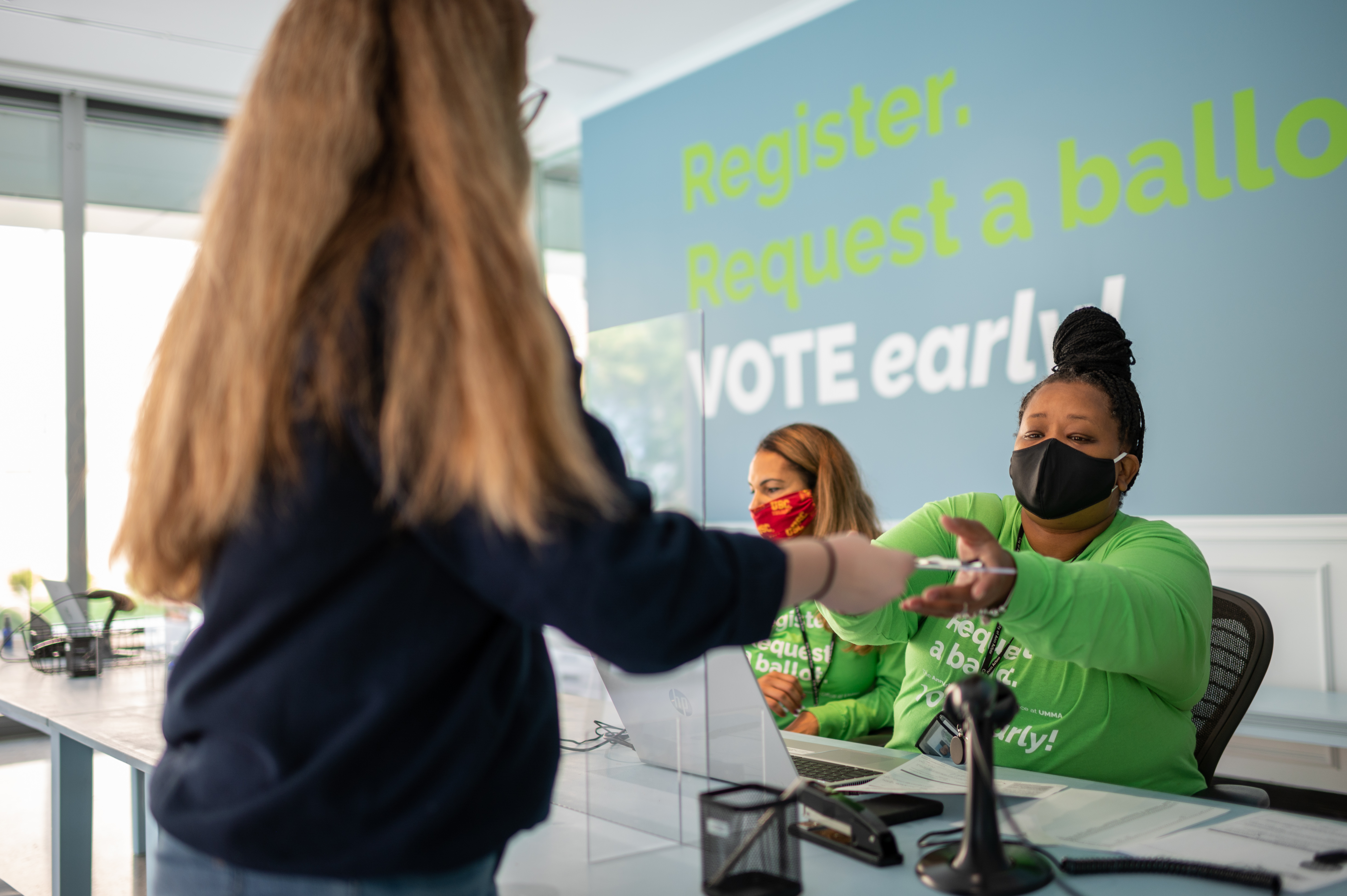 A woman hands a voter registration form to a student at the Ann Arbor City Clerk's office satellite location inside UMMA