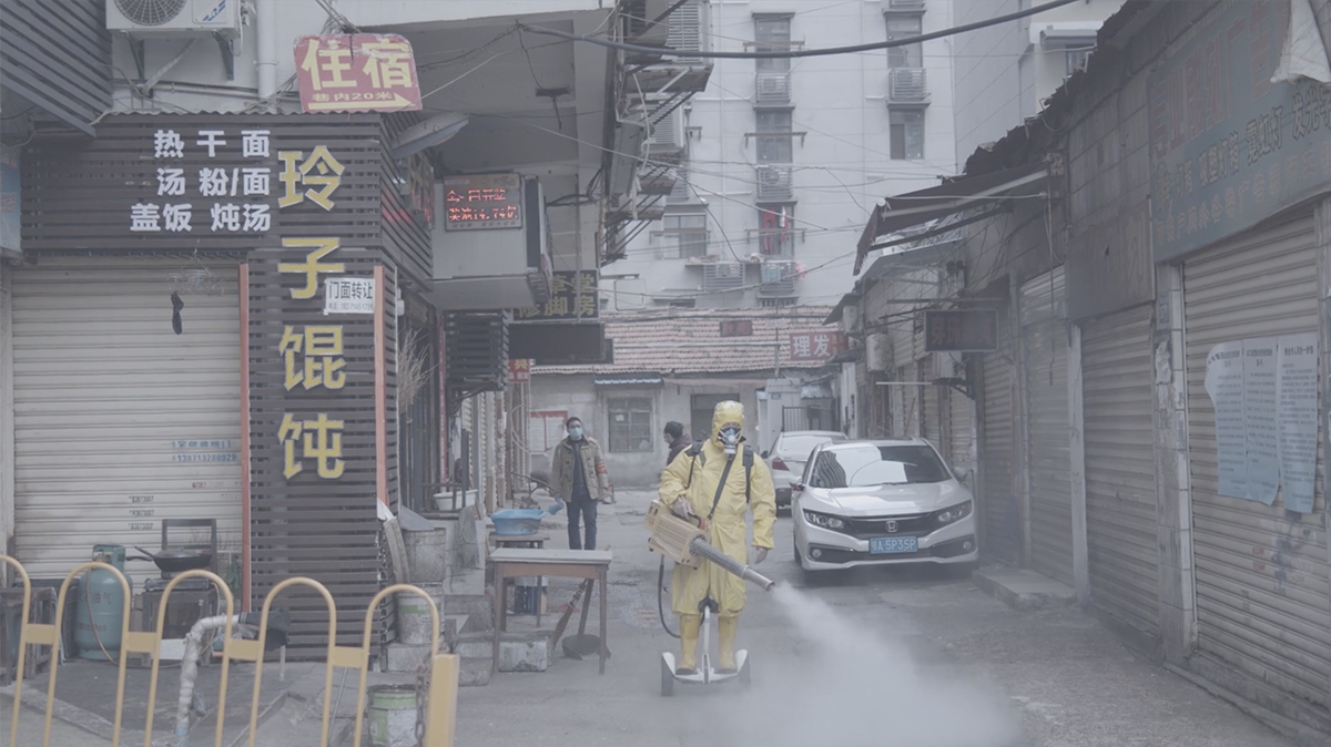 a man in a full-body yellow hazmat suit uses a device to spray disinfecting fog in the streets of China