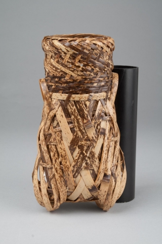 This is a basket made of light brown bamboo, with some dark brown streaks. It is shaped like a cicada, standing upright on its wings. The top is open.