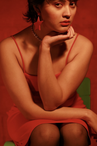 A portrait of a seated woman in a feminine pose. She is dressed in a red dress and has a dangling red star earring